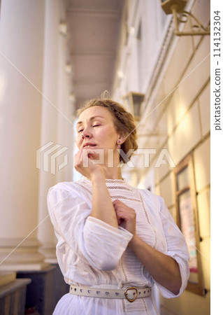 elegant middle age woman in white vintage dress near theater with antique colonnades 114132304