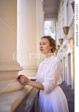 elegant middle age woman in white vintage dress near theater with antique colonnades 114132317