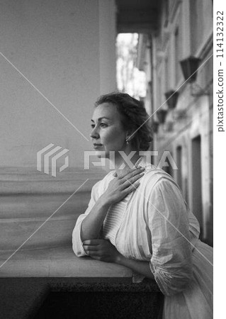 elegant middle age woman in white vintage dress near theater with antique colonnades 114132322