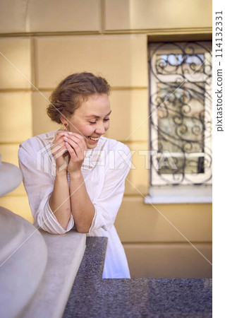 elegant middle age woman in white vintage dress near theater with antique colonnades 114132331