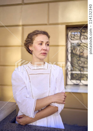 elegant middle age woman in white vintage dress near theater with antique colonnades 114132340