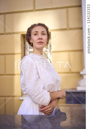 elegant middle age woman in white vintage dress near theater with antique colonnades 114132353