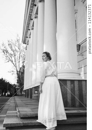 elegant middle age woman in white vintage dress near theater with antique colonnades 114132371