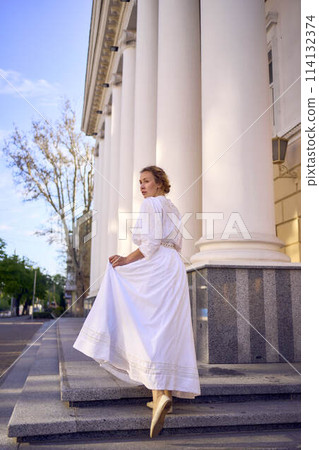 elegant middle age woman in white vintage dress near theater with antique colonnades 114132374