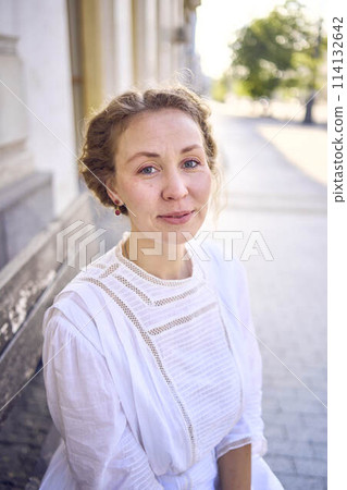 elegant middle age woman in a white vintage dress sitting on a bench in the morning city elegant middle age woman in a white vintage dress sitting on a bench in the morning city 114132642