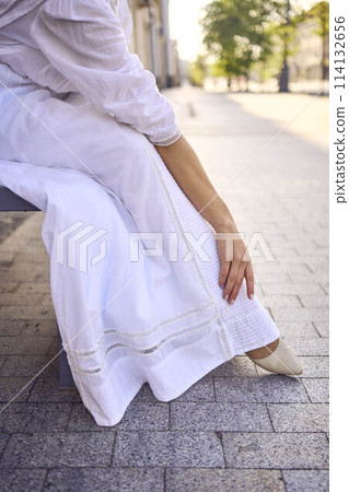 elegant middle age woman in a white vintage dress sitting on a bench in the morning city 114132656