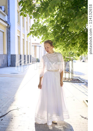 elegant middle age woman in a white vintage dress against the background of historical buildings in the morning light 114132658
