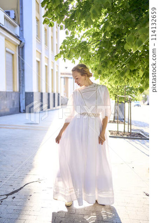 elegant middle age woman in a white vintage dress against the background of historical buildings in the morning light elegant middle age woman in a white vintage dress against the background of historical buildings in the morning light 114132659