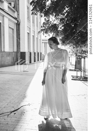 elegant middle age woman in a white vintage dress against the background of historical buildings in the morning light 114132661