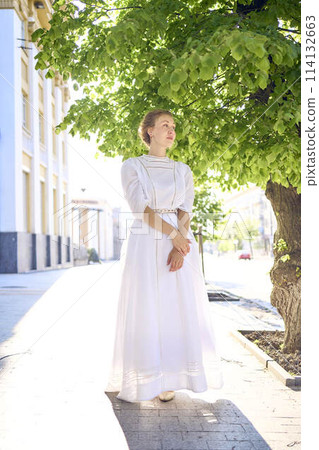 elegant middle age woman in a white vintage dress against the background of historical buildings in the morning light elegant middle age woman in a white vintage dress against the background of historical buildings in the morning light 114132663