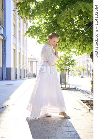 elegant middle age woman in a white vintage dress against the background of historical buildings in the morning light elegant middle age woman in a white vintage dress against the background of historical buildings in the morning light 114132664