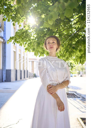 elegant middle age woman in a white vintage dress against the background of historical buildings in the morning light elegant middle age woman in a white vintage dress against the background of historical buildings in the morning light 114132665