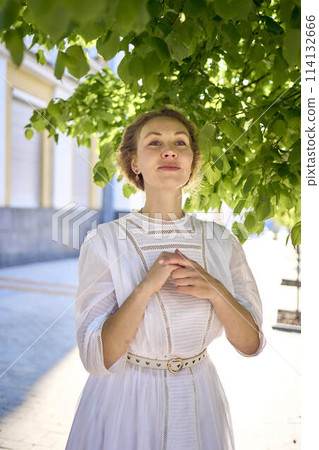 elegant middle age woman in a white vintage dress against the background of historical buildings in the morning light elegant middle age woman in a white vintage dress against the background of historical buildings in the morning light 114132666