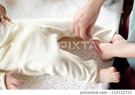 A mother dressing her little baby boy boy at home. childhood parenthood and growing up family concept real people 114132722