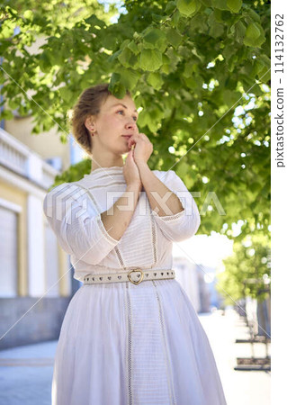 elegant middle age woman in a white vintage dress against the background of historical buildings in the morning light 114132762