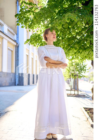 elegant middle age woman in a white vintage dress against the background of historical buildings in the morning light elegant middle age woman in a white vintage dress against the background of historical buildings in the morning light 114132763