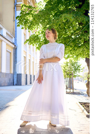 elegant middle age woman in a white vintage dress against the background of historical buildings in the morning light elegant middle age woman in a white vintage dress against the background of historical buildings in the morning light 114132765