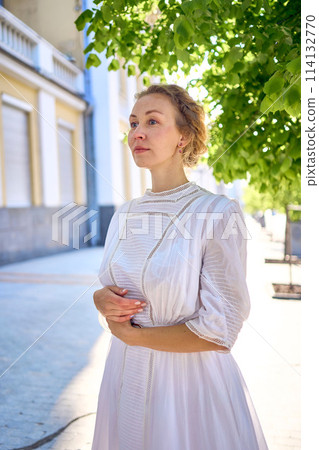 elegant middle age woman in a white vintage dress against the background of historical buildings in the morning light elegant middle age woman in a white vintage dress against the background of historical buildings in the morning light 114132770