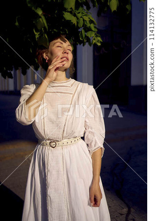 elegant middle age woman in a white vintage dress against the background of historical buildings in the morning light 114132775