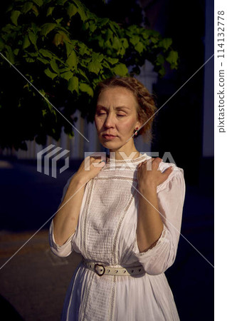 elegant middle age woman in a white vintage dress against the background of historical buildings in the morning light elegant middle age woman in a white vintage dress against the background of historical buildings in the morning light 114132778