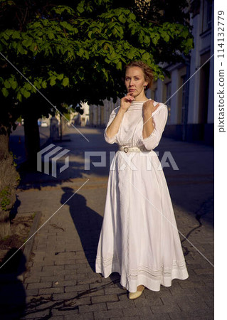 elegant middle age woman in a white vintage dress against the background of historical buildings in the morning light elegant middle age woman in a white vintage dress against the background of historical buildings in the morning light 114132779