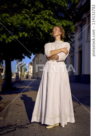 elegant middle age woman in a white vintage dress against the background of historical buildings in the morning light elegant middle age woman in a white vintage dress against the background of historical buildings in the morning light 114132782