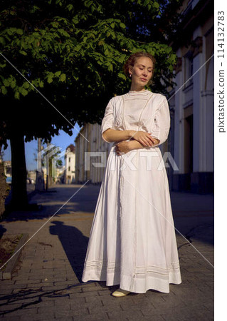 elegant middle age woman in a white vintage dress against the background of historical buildings in the morning light elegant middle age woman in a white vintage dress against the background of historical buildings in the morning light 114132783