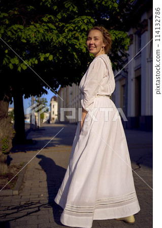 elegant middle age woman in a white vintage dress against the background of historical buildings in the morning light 114132786