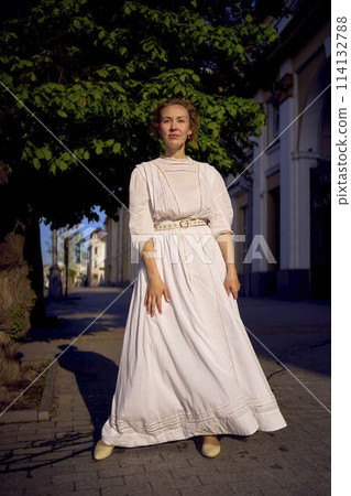 elegant middle age woman in a white vintage dress against the background of historical buildings in the morning light elegant middle age woman in a white vintage dress against the background of historical buildings in the morning light 114132788