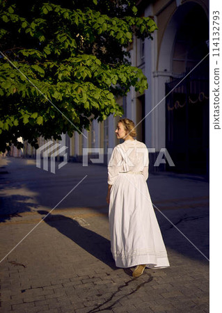 elegant middle age woman in a white vintage dress against the background of historical buildings in the morning light elegant middle age woman in a white vintage dress against the background of historical buildings in the morning light 114132793