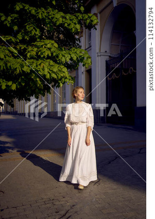 elegant middle age woman in a white vintage dress against the background of historical buildings in the morning light 114132794
