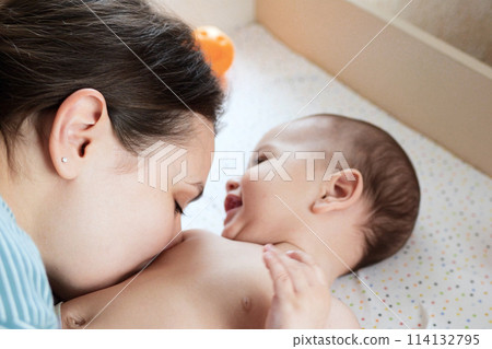 Young mother, kissing her baby boy at home. Family concept. Closeup portrait of loving mother young woman kissing little kid, home interior 114132795