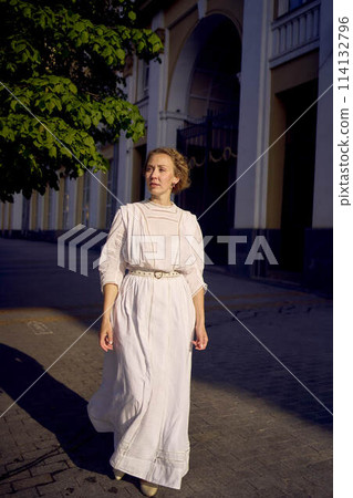 elegant middle age woman in a white vintage dress against the background of historical buildings in the morning light 114132796