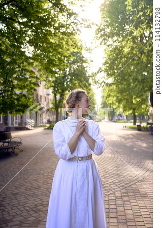 chic middle age woman in a white vintage dress in a sunlit alley 114132798