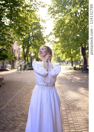 chic middle age woman in a white vintage dress in a sunlit alley chic middle age woman in a white vintage dress in a sunlit alley 114132799