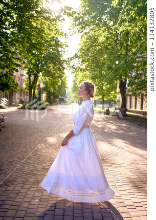 chic middle age woman in a white vintage dress in a sunlit alley 114132805
