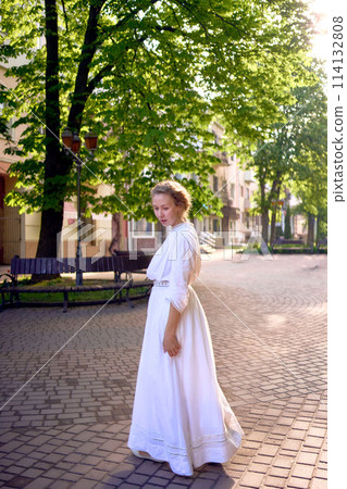 chic middle age woman in a white vintage dress in a sunlit alley 114132808