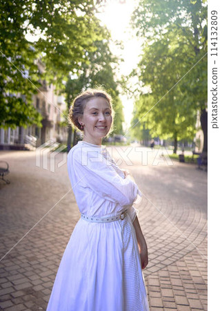 chic middle age woman in a white vintage dress in a sunlit alley chic middle age woman in a white vintage dress in a sunlit alley 114132809