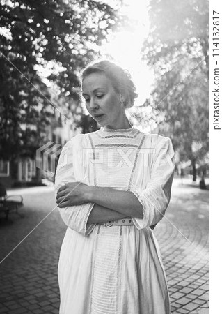 chic middle age woman in a white vintage dress in a sunlit alley 114132817