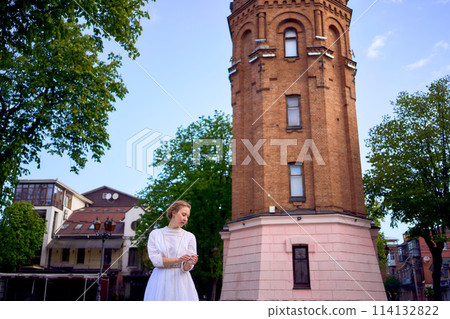 chic young woman in a white vintage dress on the square near the historic water tower in Vinnytsia chic young woman in a white vintage dress on the square near the historic water tower in Vinnytsia 114132822