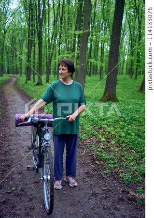 elderly woman walking in spring forest with bicycle and yoga mat 114133078