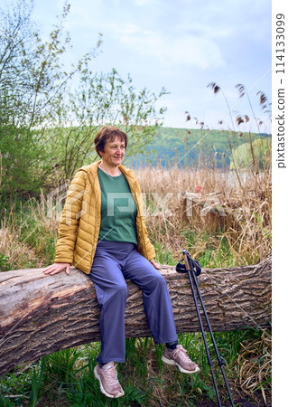 elderly woman rests on the river bank after Nordic walking exercise elderly woman rests on the river bank after Nordic walking exercise 114133099