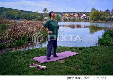 old woman doing exercises in the morning on the river bank, a bicycle and a yogamat next to her old woman doing exercises in the morning on the river bank, a bicycle and a yogamat next to her 114133122