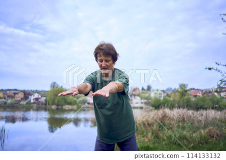 old woman doing exercises in the morning on the river bank, a bicycle and a yogamat next to her old woman doing exercises in the morning on the river bank, a bicycle and a yogamat next to her 114133132