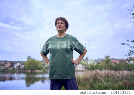 old woman doing exercises in the morning on the river bank, a bicycle and a yogamat next to her 114133133