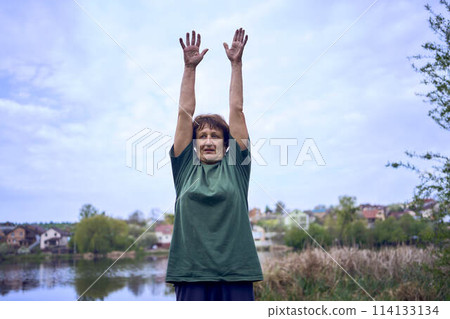 old woman doing exercises in the morning on the river bank, a bicycle and a yogamat next to her old woman doing exercises in the morning on the river bank, a bicycle and a yogamat next to her 114133134