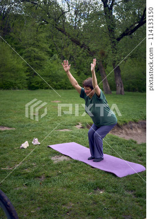 old woman practices yoga in the morning on the river bank, came from home by bicycle old woman practices yoga in the morning on the river bank, came from home by bicycle 114133150