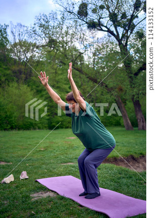 old woman practices yoga in the morning on the river bank, came from home by bicycle old woman practices yoga in the morning on the river bank, came from home by bicycle 114133152
