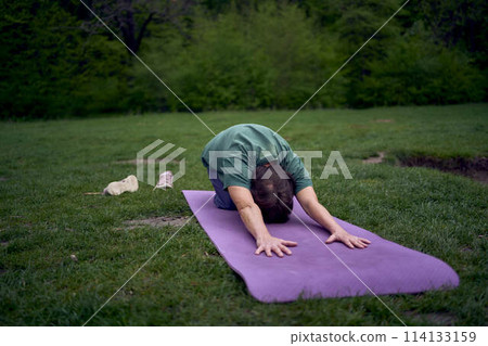 old woman practices yoga in the morning on the river bank, came from home by bicycle 114133159