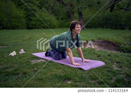 old woman practices yoga in the morning on the river bank, came from home by bicycle 114133164